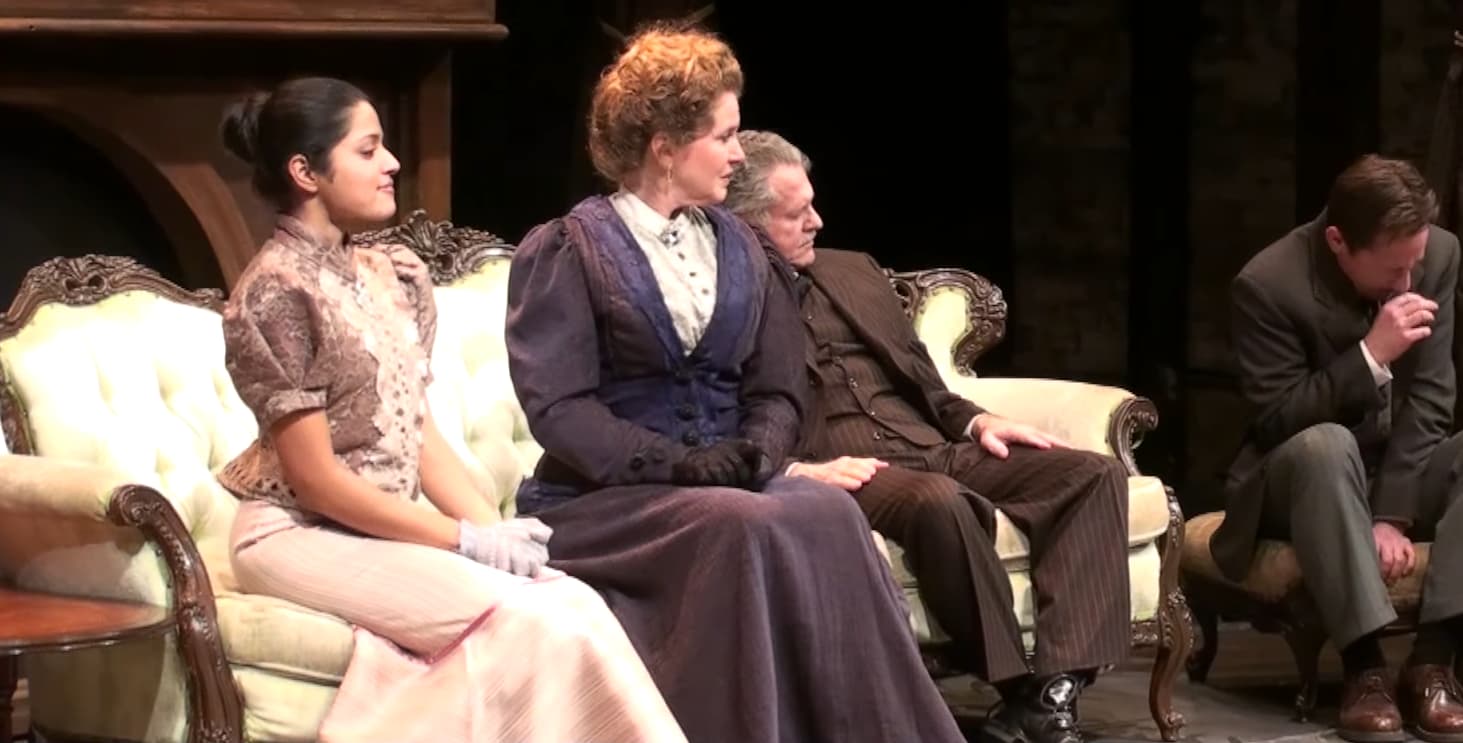 Four actors on stage in a Victorian-era play setting