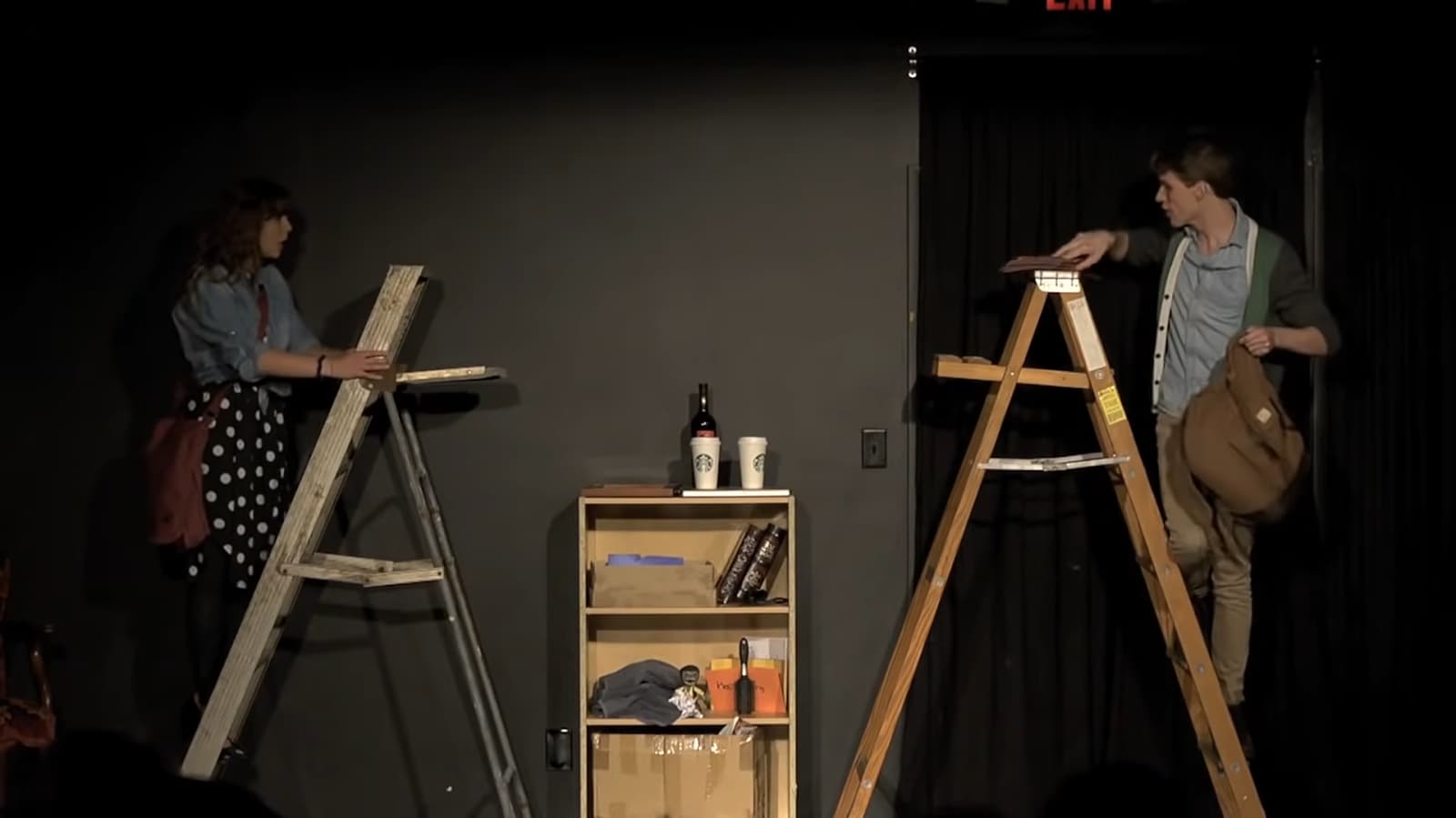 Two actors on ladders face each other on a dimly lit stage