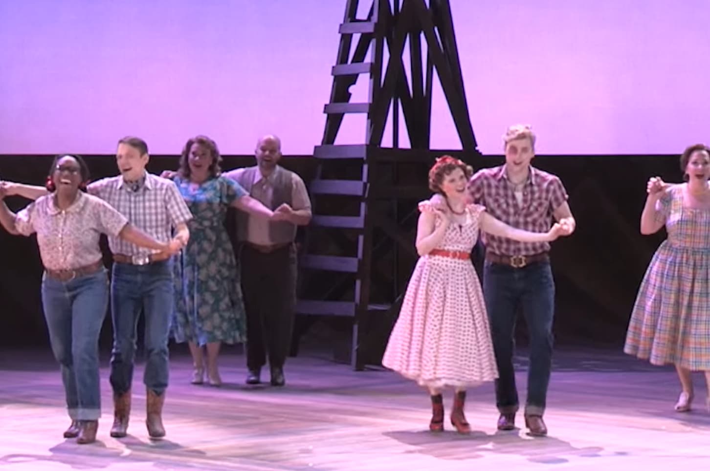 A group of six performers are dancing on stage in a musical theater production