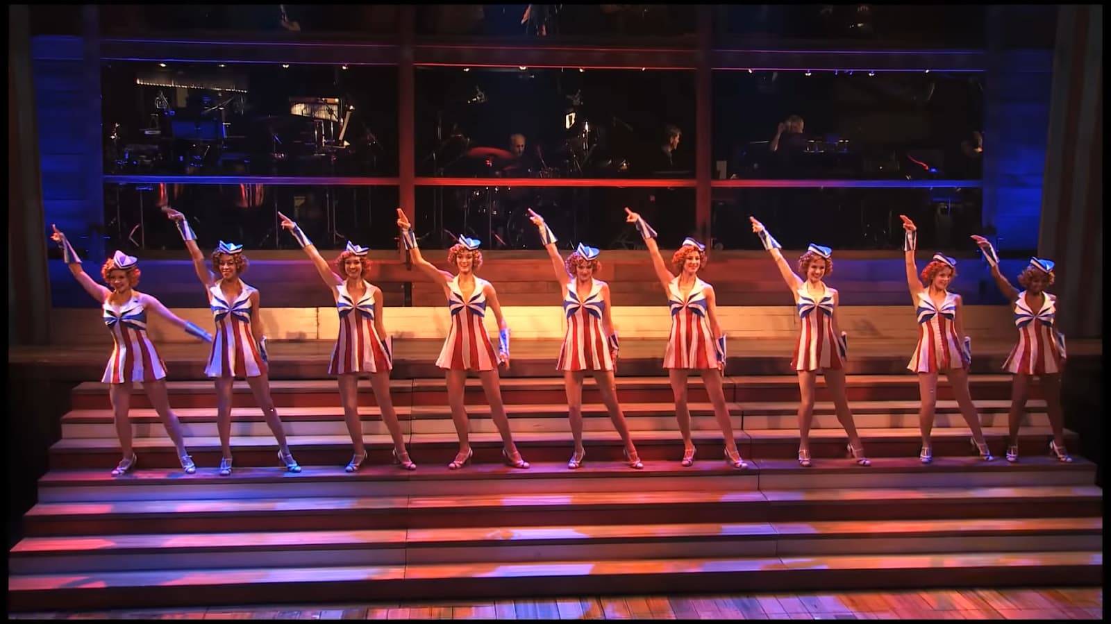 A group of performers in sailor-themed outfits strike a pose on stage