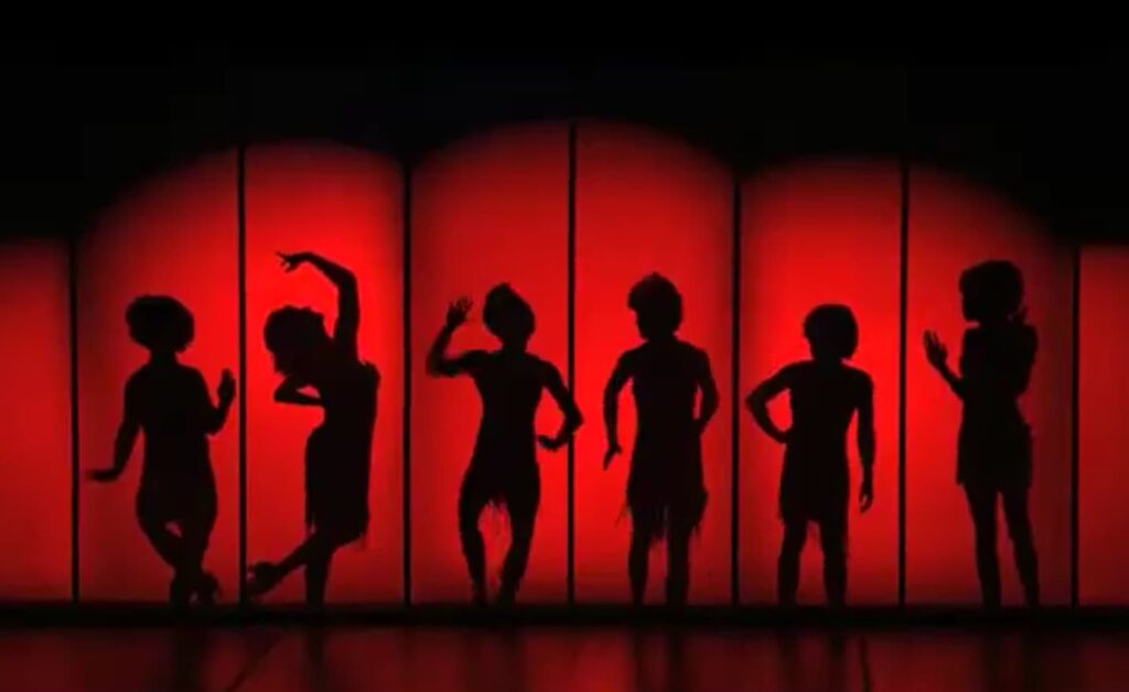 Silhouettes of six dancers behind a red screen striking dynamic poses
