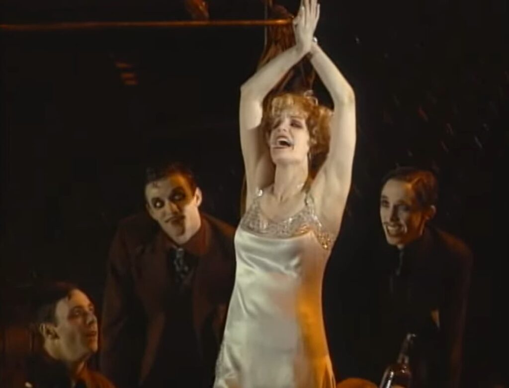 A woman joyously performs on stage, surrounded by admiring men