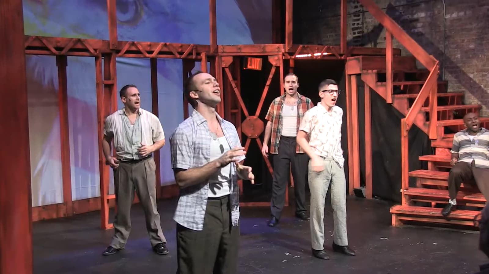 Four actors singing on stage with a wooden set design