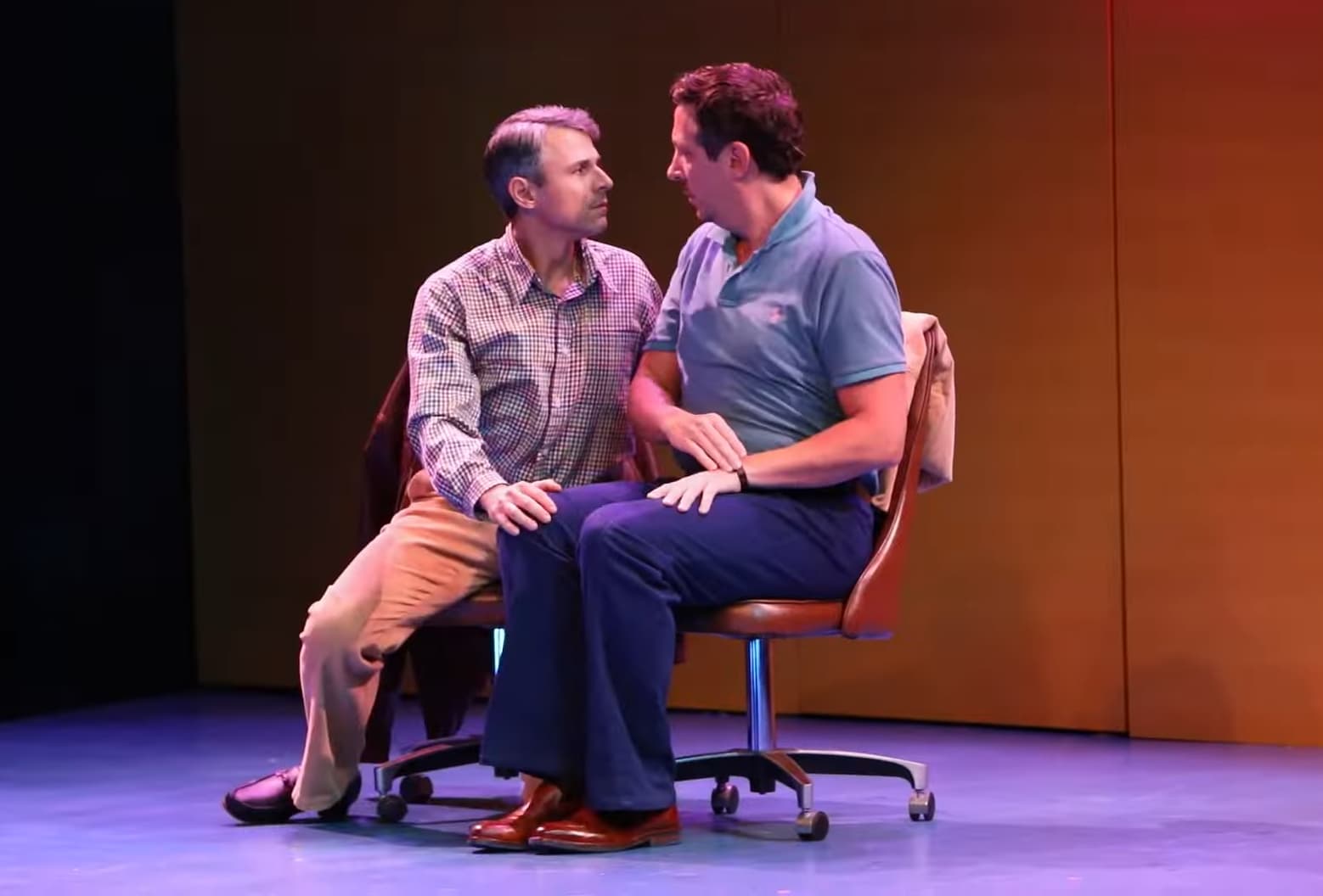 Two men sitting closely and looking at each other on a stage