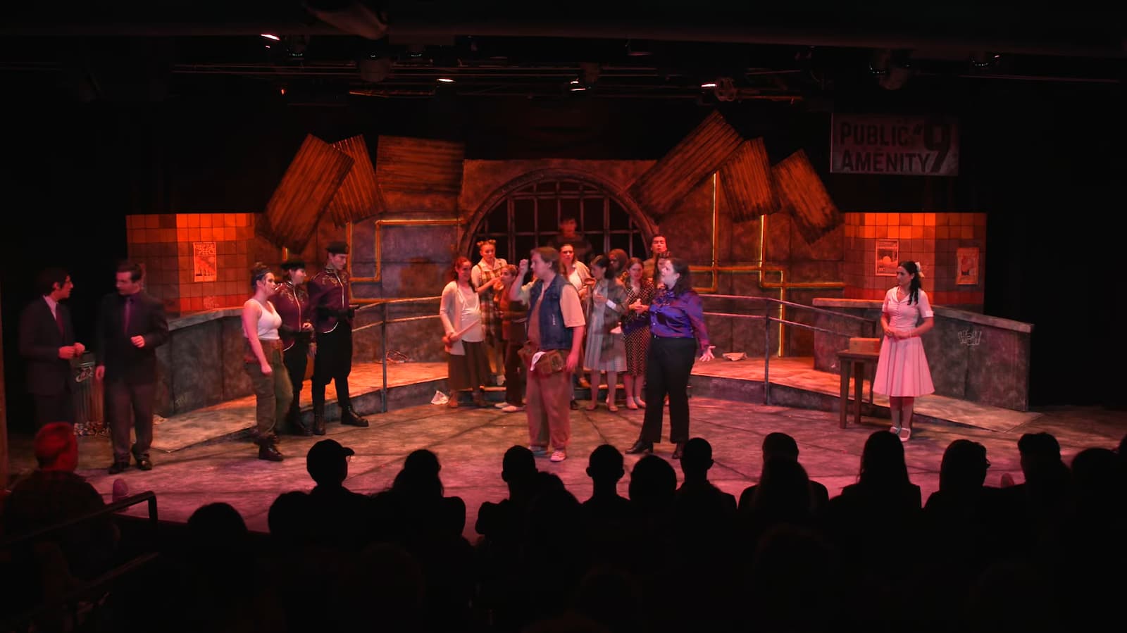 A theatrical cast performs in a rustic, dilapidated set