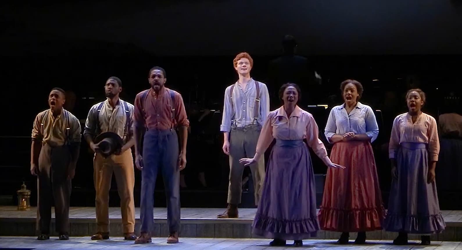 A group of performers sings on stage in a theatrical production